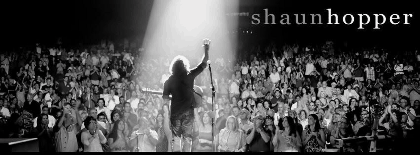 Shaun Hopper standing beneath a spotlight before a full theater audience